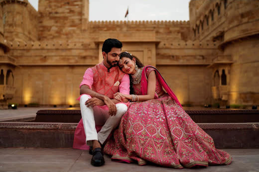A couple in pink seated on steps inside a lamplit sandstone fort
