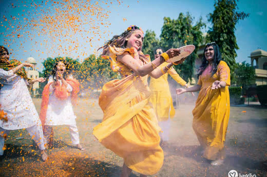 Women in yellow dancing through a cloud of flower petals at a haldi