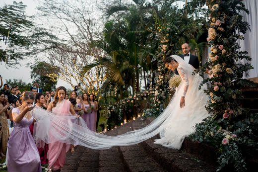 A bride’s long white veil carried down a candlelit garden aisle