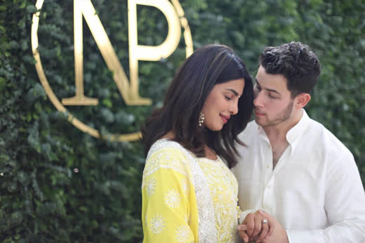 Priyanka and Nick in front of a gold monogram on a wall of green