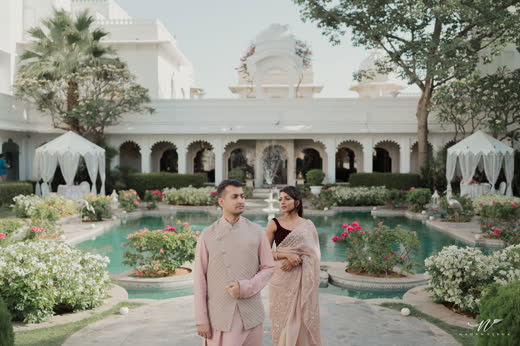 A couple walking beside a palace courtyard pool lined with white canopies