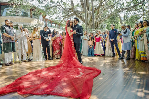 A bride in a long red trail dancing with the groom while guests watch
